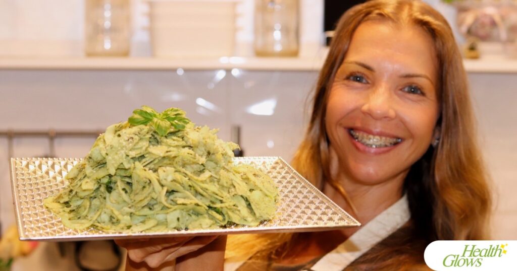 Marina from Health Glows holding a plate with raw vegan fusilli al pesto pasta.
