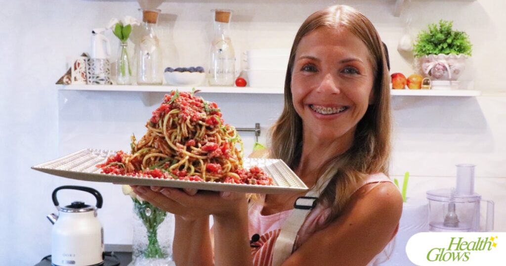 Marina from Health Glows holding a plate with raw vegan spaghetti marinara pasta.