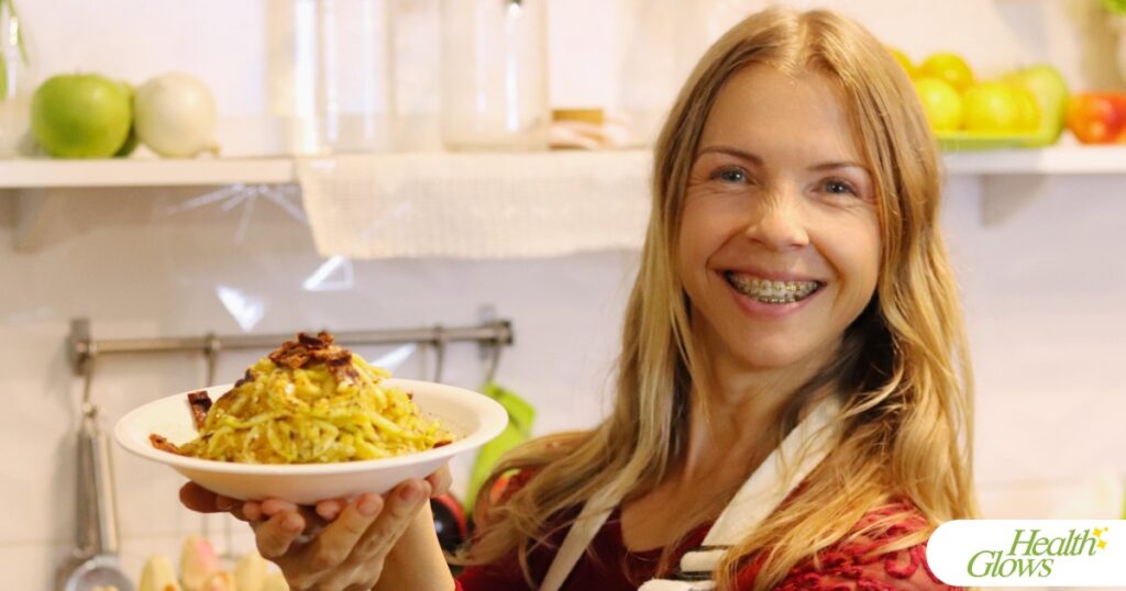 Marina from Health Glows is holding a plate with raw vegan spaghettoni carbonara pasta.