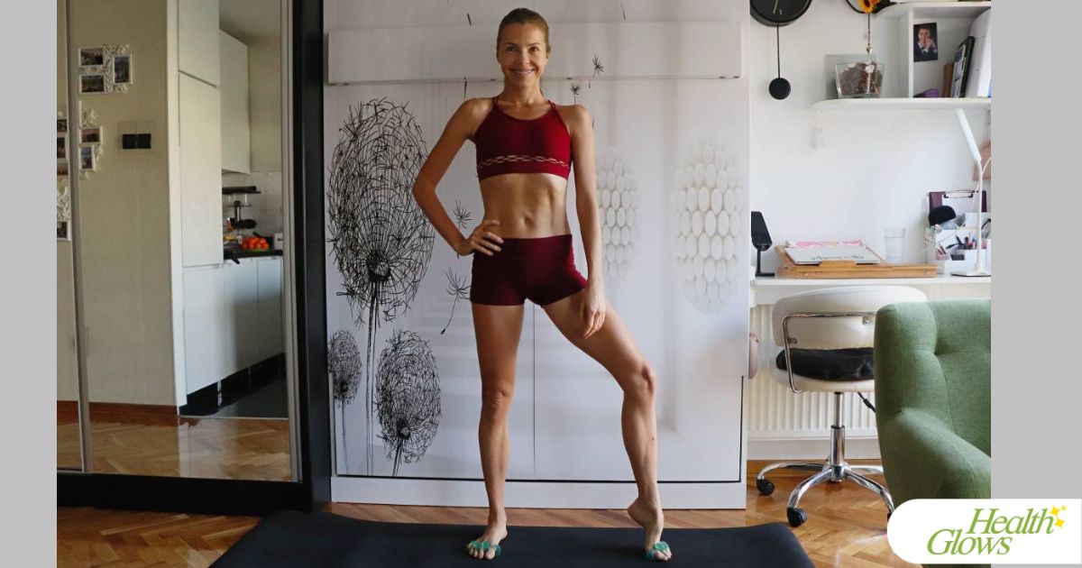 Marina from Health Glows, standing on a yoga mat in a dark red yoga outfit.