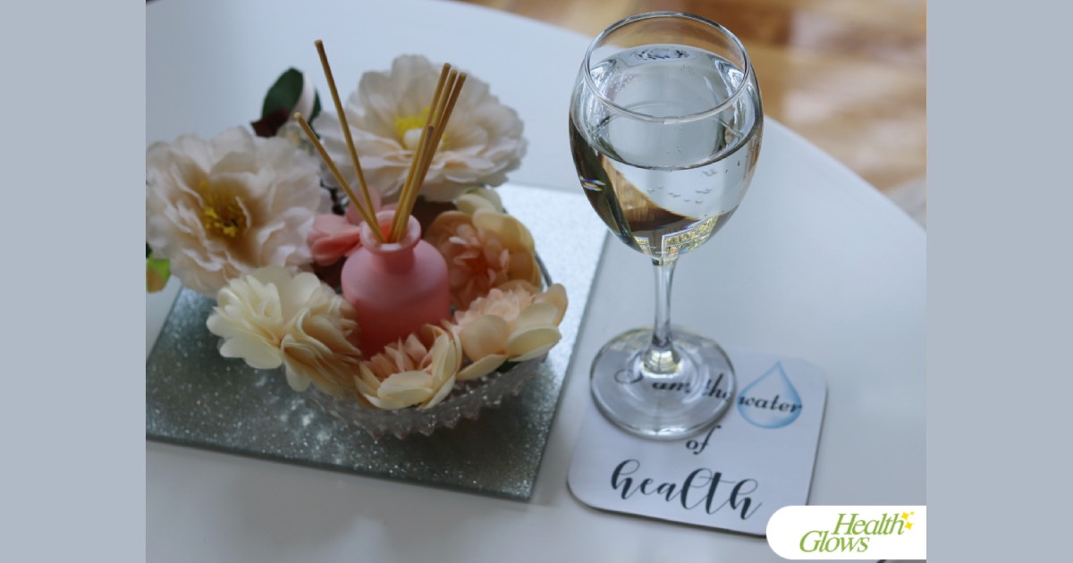 A wine glass filled with clean water on a coaster that reads 'I Am the Water of Health'. Next to it is a silver coaster with decorative flowers and incense sticks in a glass bowl.
