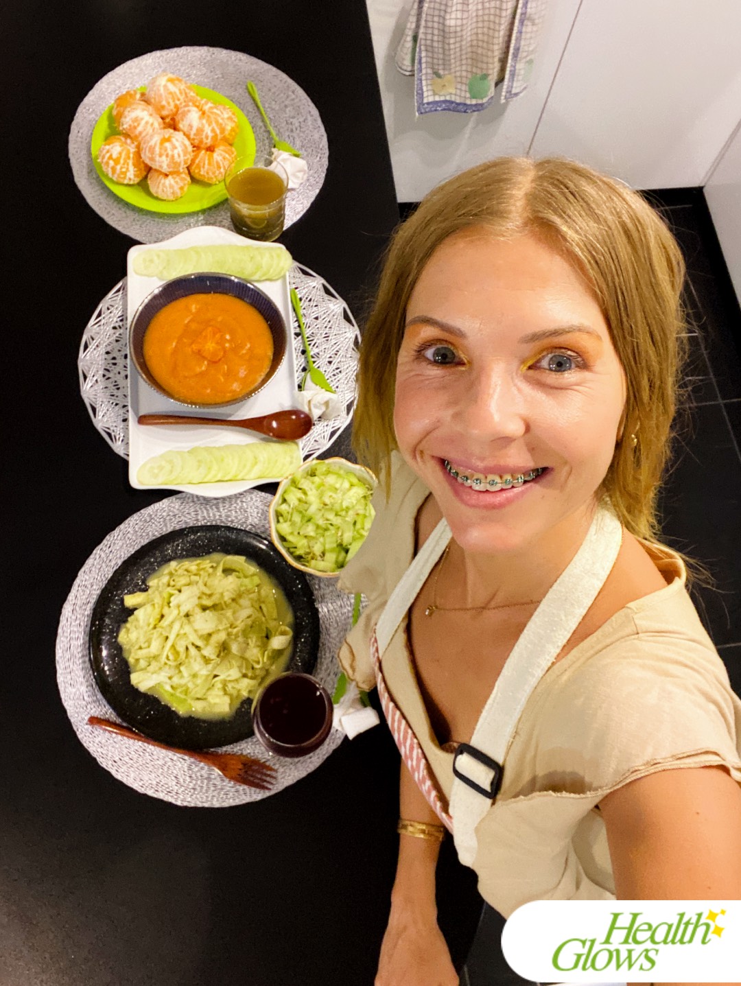 Marina from Health Glows standing next to her kitchen counter where three raw vegan meals are laid out: breakfast, lunch and dinner.