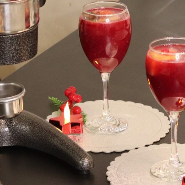 A pomegranate press standing next to two wine glasses filled with pomegranate juice.