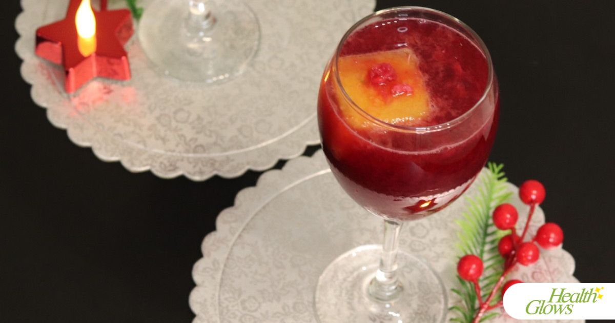 A wine glass filled with pomegranate juice and an orange juice ice cube inside, pictured from above.