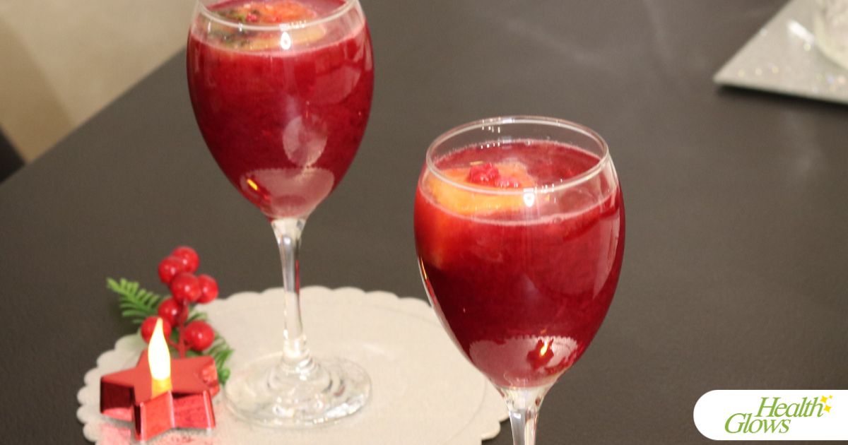 Two wine glasses filled with pomegranate juice and decorated with a festive candle and some berries.
