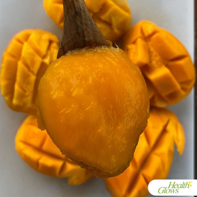 Mango flesh in a spoon. There are open mango halves behind the spoon.