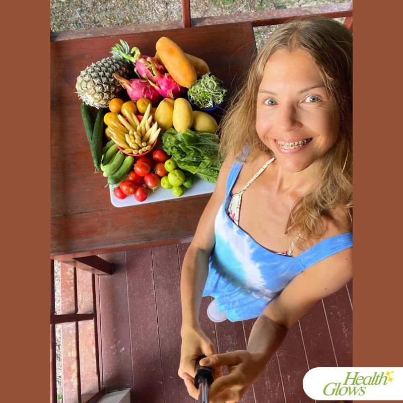 Marina from Health Glows standing next to a table filled with various tropical fruits.