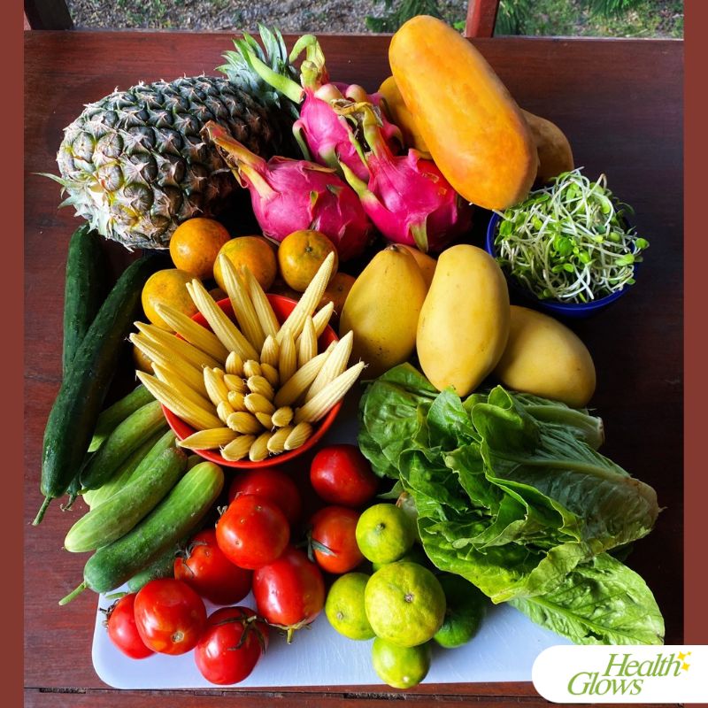 Table filled with various tropical fruits ande vegetables: pineapple, dragon fruit, papaya, sunflower sprouts, mangoes, tangerines, cucumbers, baby corns, Romaine lettuce, limes, tomatoes.