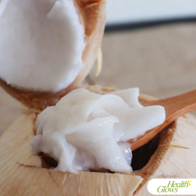 Young coconut flesh in a spoon above an open Thai coconut.