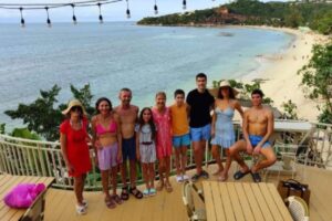 The Health Glows Thai Retreat 2025 group standing on a bar balcony, with the sea and the beach in the background.