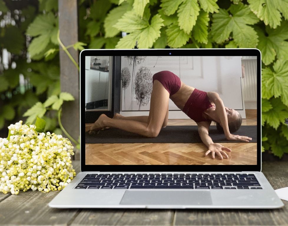 Marina from Health Glows demonstrates the 'Thread the Needle' yoga pose ('Urdhva Mukha Pasasana') on a laptop screen.