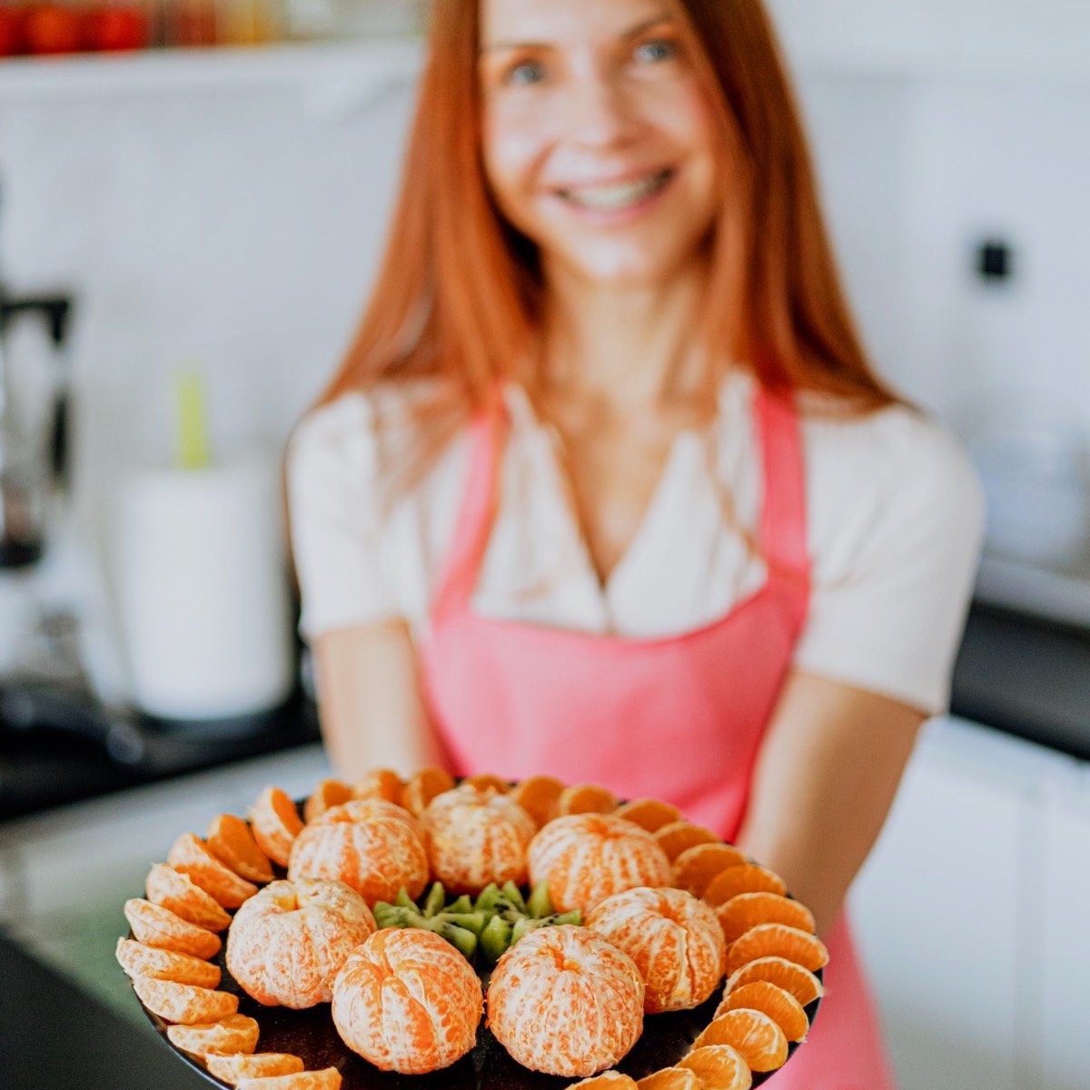 Marina from Health Glows smiling and holding a plate filled with tangerines and kiwis.