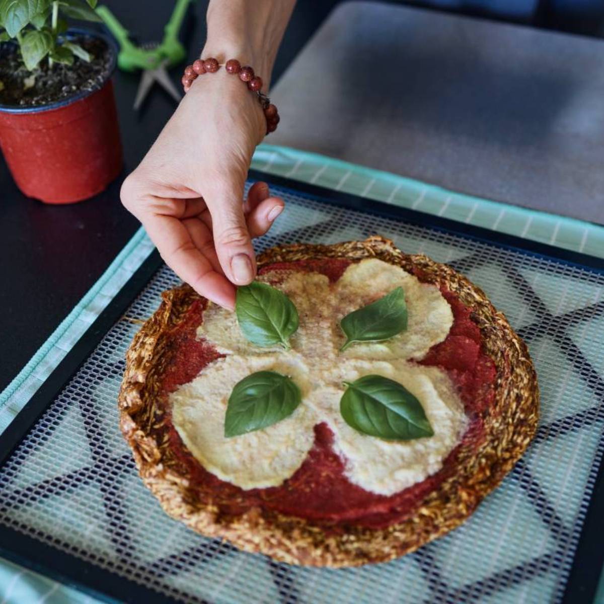 Marina from Health Glows is putting a basil leaf on a raw vegan pizza.