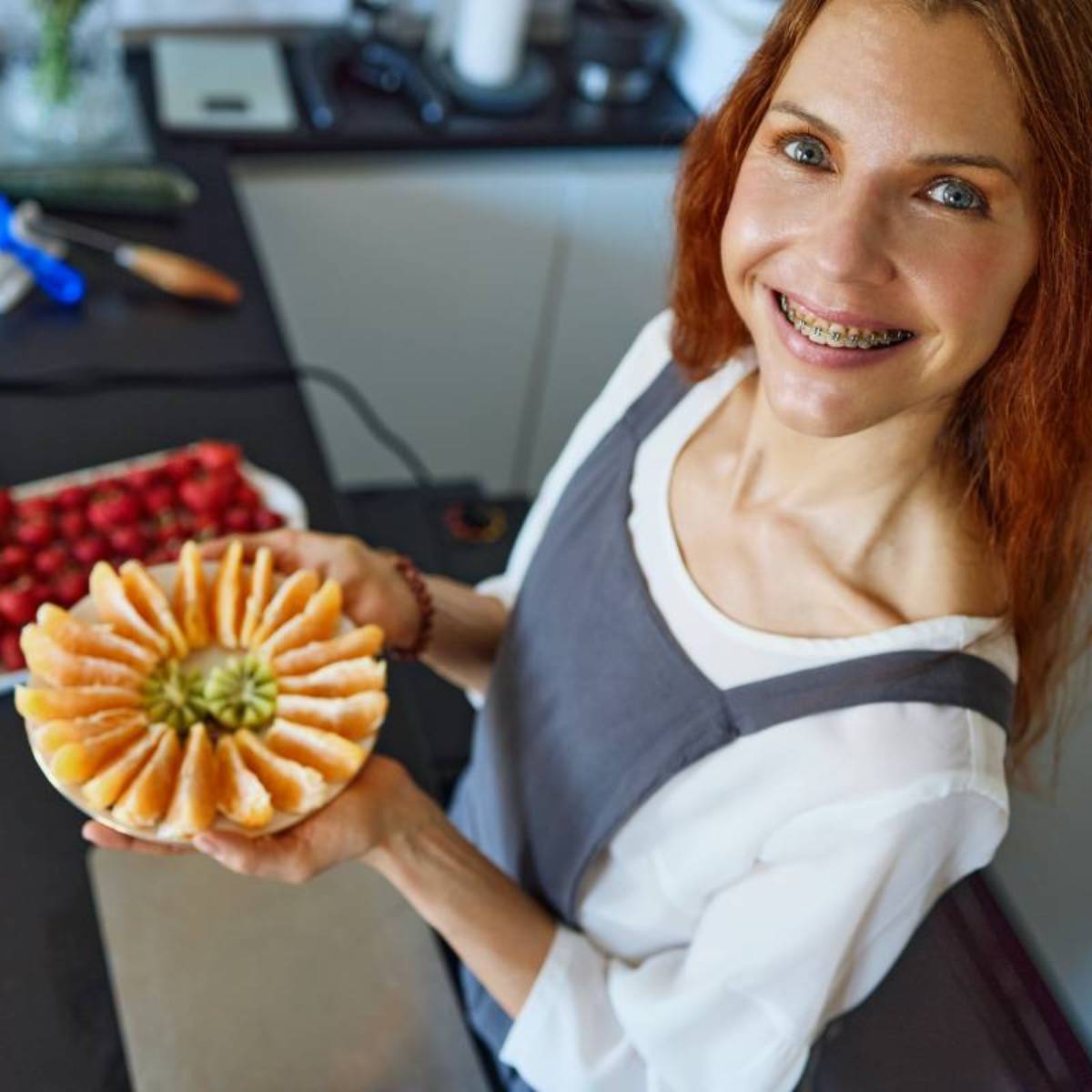 Marina from Health Glows is holding a plate with peeled orange slices arranged in a circle and two halves of a kiwi in the middle of the plate.